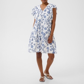 Model wearing Kaffe Chalk Midnight Flower mini dress with ruffle detail and V-neck, styled with white strappy sandals.