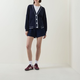 Model wearing Varley navy knit cardigan with white contrast trim, styled with matching navy shorts and burgundy trainers