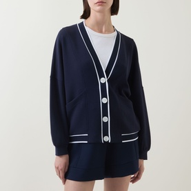 Model wearing Varley navy cardigan with white contrast trim, button front and patch pockets, styled with matching navy shorts