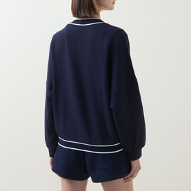 Model wearing Varley navy knitwear sweatshirt with white tipping trim, shown from behind, styled with matching navy shorts.