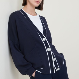 Model wearing Varley navy cardigan with white contrast trim, button front and V-neckline, styled with a white crew neck top.
