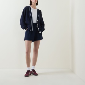 Model wearing Varley navy knit cardigan with white trim, styled with matching navy shorts and burgundy trainers
