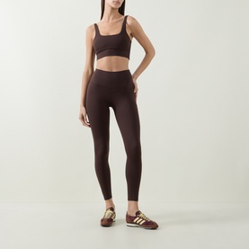 Model wearing Varley Coffee Bean leggings with matching sports bra and gold-stripe trainers.