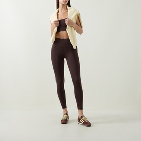 Model wearing Varley Coffee Bean leggings with matching crop top, styled with a cream vest and gold-striped trainers