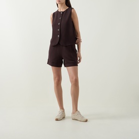 Model wearing Varley Coffee Bean shorts in viscose blend, styled with matching sleeveless waistcoat and cream trainers.