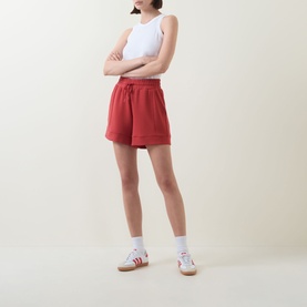 Model wearing red drawstring shorts with white sleeveless top, white socks and striped trainers