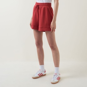 Model wearing red fleece shorts with elasticated waist and side pockets, styled with white socks and red Adidas trainers
