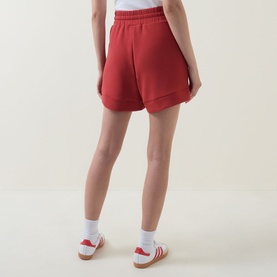 Model wearing red high-waisted shorts, styled with white socks and red and white trainers, rear view