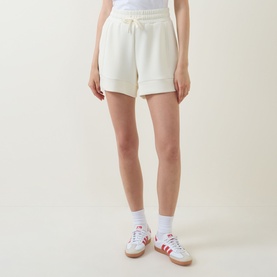 Model wearing Varley Pristine shorts in off-white with elasticated drawstring waist and cuffed hem, styled with white socks and trainers.