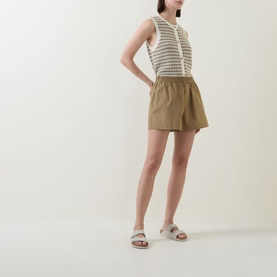 Model wearing Varley Golden Olive cotton shorts with elasticated waist, styled with a striped knit top and white slide sandals.