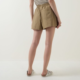 Model wearing Varley Golden Olive cotton shorts with elasticated waist, rear view, styled with silver flat shoes