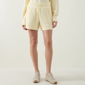Model wearing Varley shorts in Anise Flower, a soft cream hue, styled with a matching sweatshirt and beige trainers.