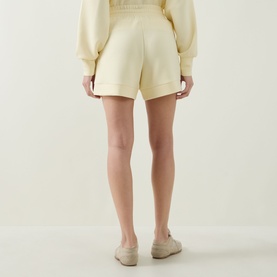 Model wearing Varley shorts in Anise Flower, pale yellow relaxed fit, styled with matching sweatshirt and nude loafers, rear view.