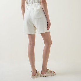 Model wearing Varley Pristine shorts, rear view, with beige buckle sandals. Elasticated waistband, relaxed fit.
