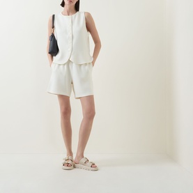 Model wearing Varley Pristine shorts with matching sleeveless top, styled with beige chunky sandals and black crossbody bag.