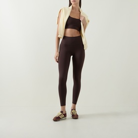 Model wearing Varley Coffee Bean Sports Bra, styled with matching dark brown leggings, cream zip-up jacket and brown trainers.