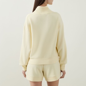 Model wearing Varley Anise Flower Sweat Top, back view, styled with matching shorts in the same pale yellow tone.