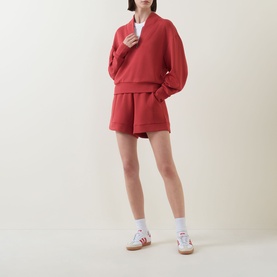 Model wearing Varley Davidson Half-Zip Sweatshirt in bossa nova with matching red shorts, white socks and colourful trainers.
