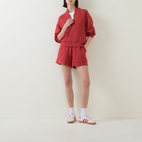 Model wearing Varley Davidson Half-Zip Sweatshirt in bossa nova with matching red shorts and white Adidas Gazelle trainers.