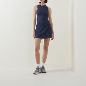 Model wearing Varley Blue Nights tank top with white tipping detail, styled with matching mini skirt and grey trainers.