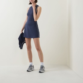 Model wearing Varley Blue Nights tank top with matching mini skirt, styled with grey trainers and a navy zip-up jacket.