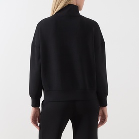Model wearing Varley black sweatshirt, shown from behind, featuring a mock neck, zip detail, and relaxed fit with matching black trousers.