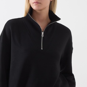 Model wearing Varley black half-zip sweatshirt with funnel neck and silver zip detail, close-up shot.