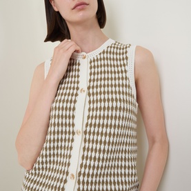 Model wearing Varley Aura Sweater Vest in Egret/Golden Olive, sleeveless knit with diamond check pattern and button fastenings, round neckline