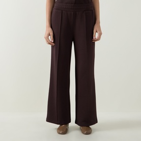 Model wearing Varley Coffee Bean wide-leg trousers with elasticated waistband, styled with tan flat shoes.