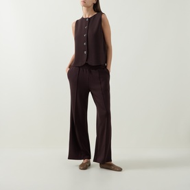 Model wearing Varley Coffee Bean trousers with matching sleeveless button vest and brown flat shoes.
