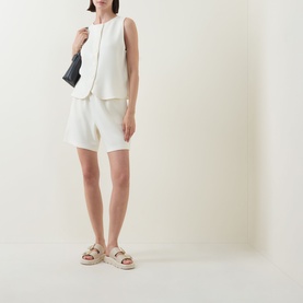 Model wearing Varley top in Pristine, styled with matching white shorts, black bag, and tan flatform sandals.