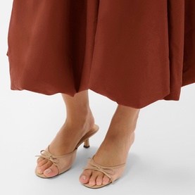 Model wearing Kaffe heeled mule sandals in nude, featuring bow detail and kitten heel, styled with a henna-toned midi skirt.