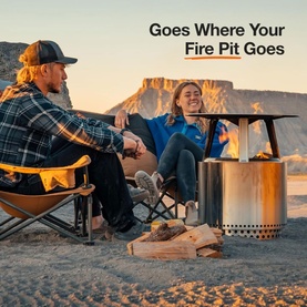 Solo Stove Bonfire Heat Deflector in outdoor desert setting with two people seated around a fire pit on sandy ground.