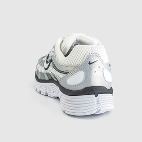 Nike trainer in white and off-white with silver mesh panelling, black Swoosh logo, and chunky white sole, rear three-quarter view