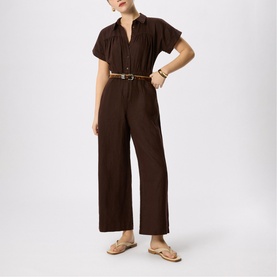 Model wearing Whistles brown short-sleeve wide-leg jumpsuit with collared V-neckline, styled with a tan belt and nude flat sandals.