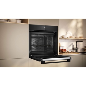 Neff black built-in single oven with open door, installed in a modern beige kitchen with open shelving and dark tap visible.