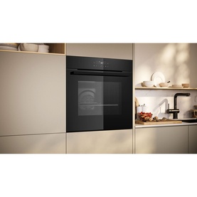 Neff black built-in single oven installed in cream cabinetry, shown in a modern kitchen setting with open shelving