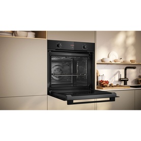 Neff black built-in single electric oven with open door, installed in fitted kitchen cabinetry with worktop and sink in background