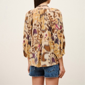 Model wearing Bash yellow ikat-print blouse with balloon sleeves, styled with blue denim shorts, rear view.