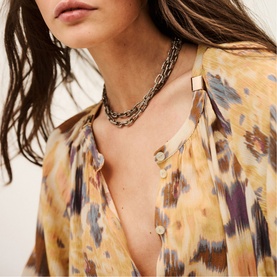 Model wearing Bash yellow abstract print sheer blouse with button detail, styled with layered gold and silver chain necklaces