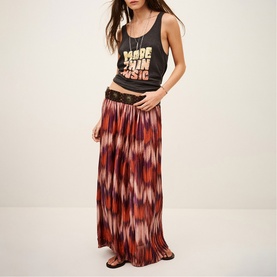 Model wearing Bash orange ikat-print maxi skirt with black graphic tank top and flat sandals.