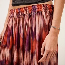 Model wearing Bash orange pleated midi skirt with ikat-style print in red, purple and orange tones, styled with a silver bracelet