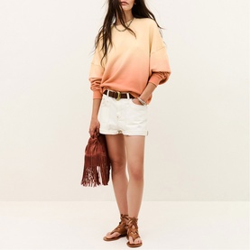 Model wearing Bash yellow ombre sweatshirt with white denim shorts, styled with brown fringe bag and tan lace-up sandals