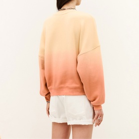 Model wearing Bash yellow ombre sweatshirt with gradient fade to coral, styled with white shorts. Back view.