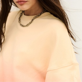 Model wearing Bash yellow sweatshirt with gradient coral hem detail, styled with a chunky chain-link necklace.