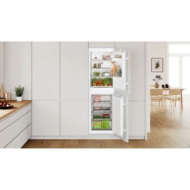 Bosch integrated fridge freezer, white, built-in to kitchen cabinetry, open door showing fully stocked shelves and freezer drawer