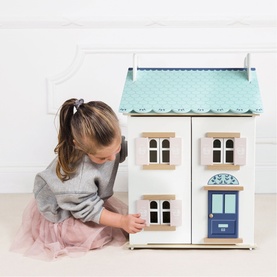 Young girl playing with Le Toy Van Daisylane wooden dolls house, white with mint blue roof, pink shutters and blue front door