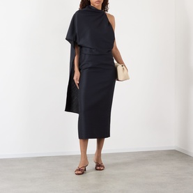 Model wearing Rohe Cape Pencil Dress in Night, midi length with asymmetric cape sleeve, styled with tan slides and small cream bag.