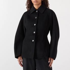 Model wearing Rohe Double-Faced Sculptural Jacket in black with cinched waist, oversized sleeves and pointed collar, styled with black trousers.