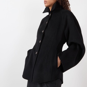 Model wearing Rohe Double-Faced Sculptural Jacket in black with pointed collar, oversized sleeves, cinched waist and button fastening.